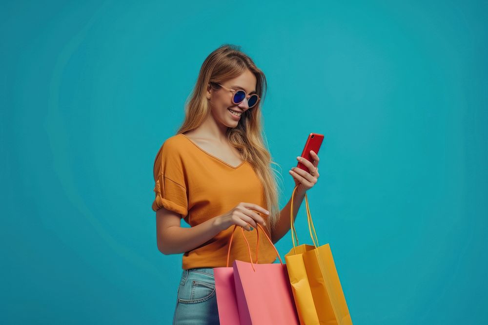 Smiling young lady wear sunglasses using her smartphone while shopping adult red bag.