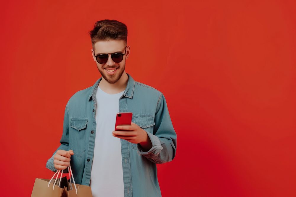 Smiling young man wear sunglasses using her smartphone adult red shopping bag.