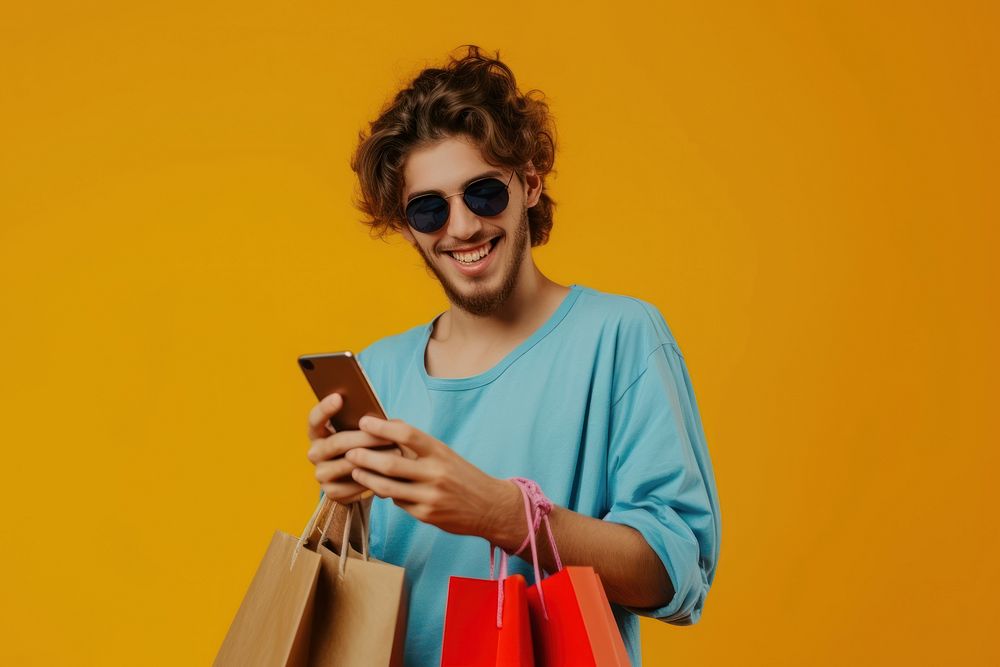 Smiling young man wear sunglasses using her smartphone bag shopping bag portability.