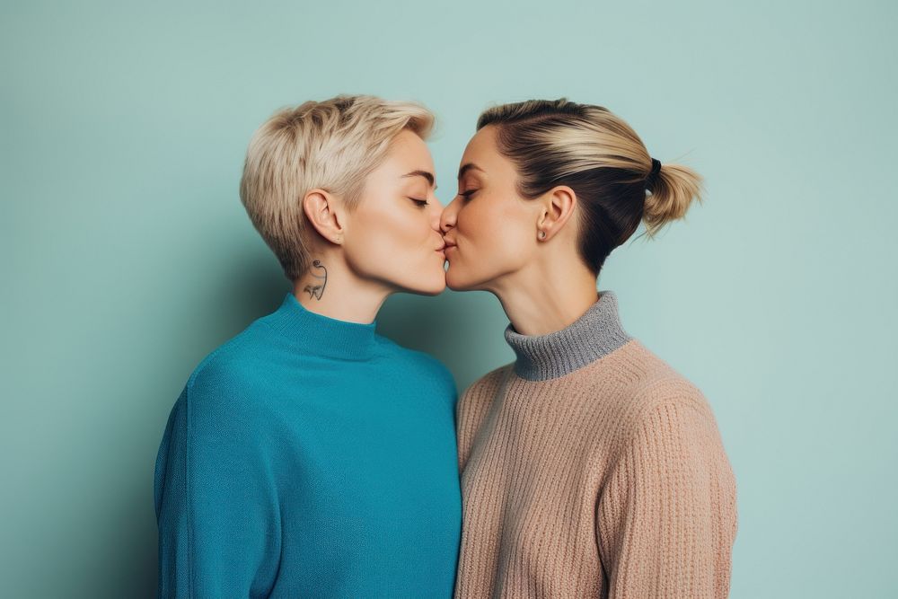 A lesbian couple wearing colorful sweater kissing adult blue.