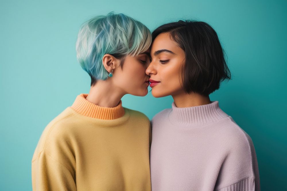 A lesbian couple wearing colorful sweater kissing adult blue.