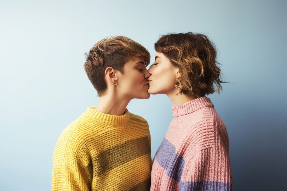 A lesbian couple wearing colorful sweater kissing blue affectionate.