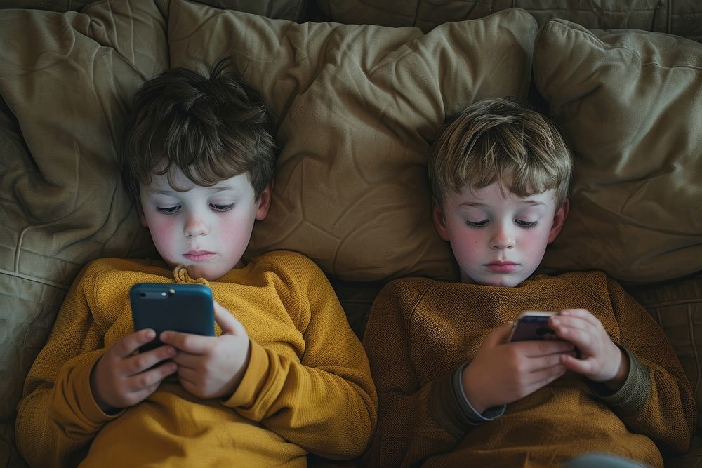 Two boys are laying on a couch with their phone photography furniture portrait.