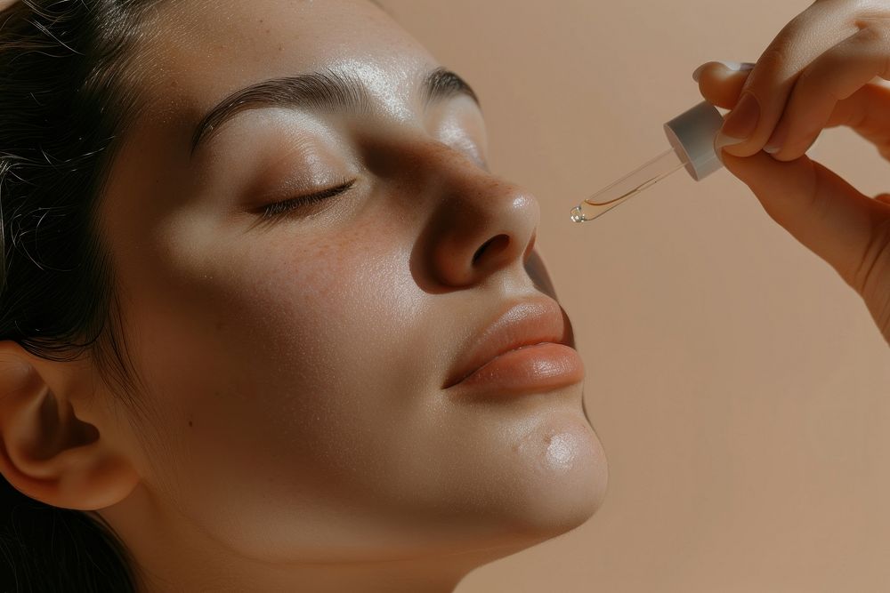 Woman applying facial serum drops cosmetics adult skin.