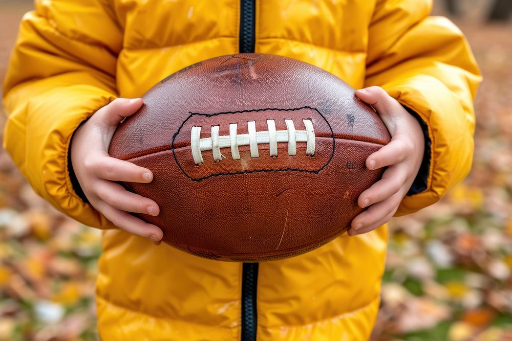 A kid holding American football ball sports american football midsection.