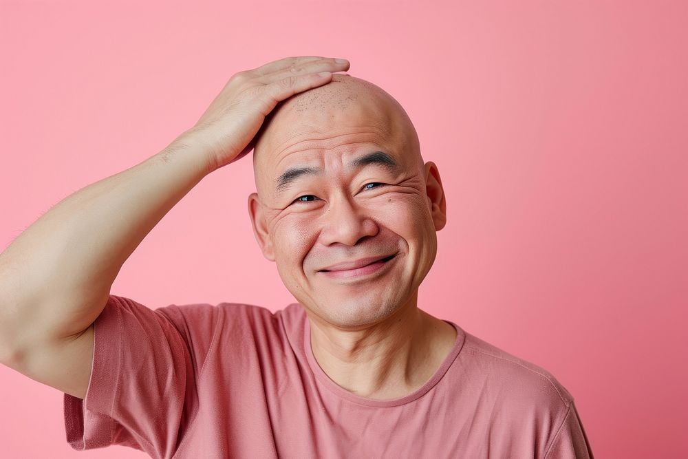 Bald middle age asian man touching shaved head smile frustration happiness.
