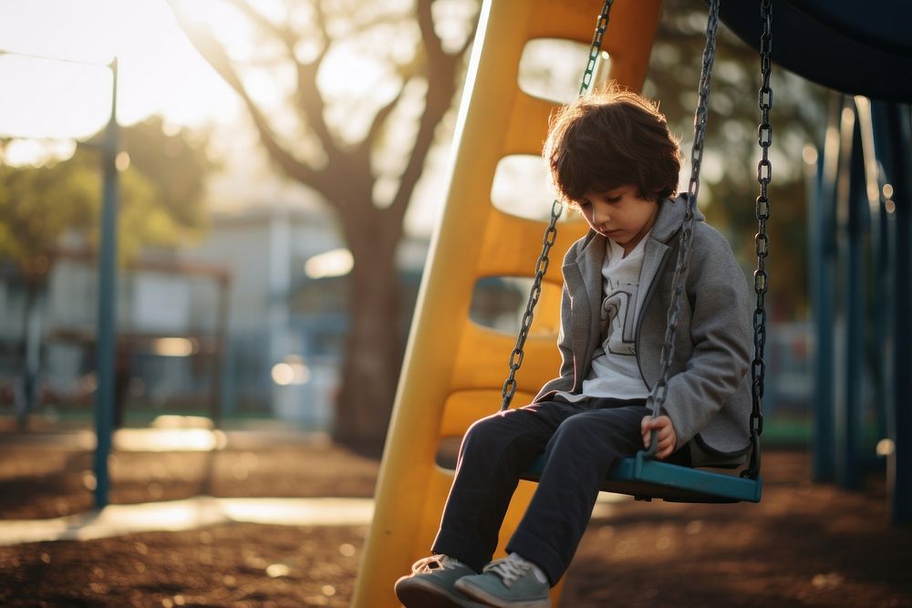 A kid with autism playing in the playground outdoors sitting looking.