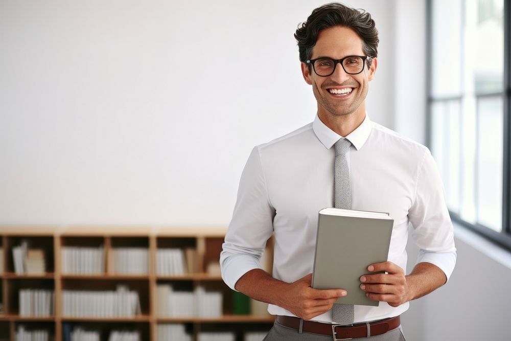 Smiling teacher holding book glasses smiling shirt.