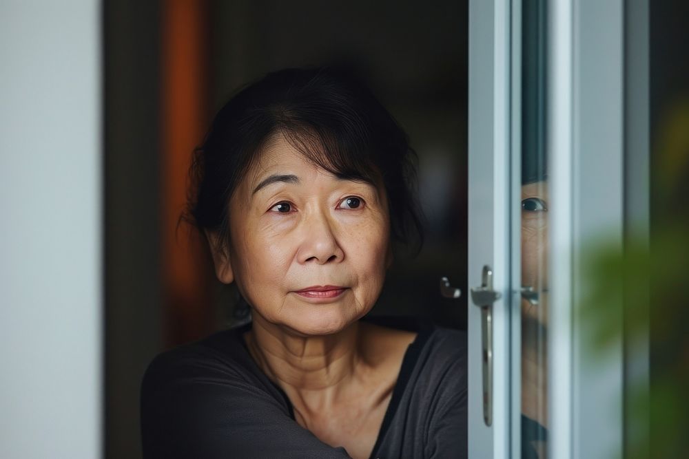 Asian mature woman looking over the door worried adult contemplation.