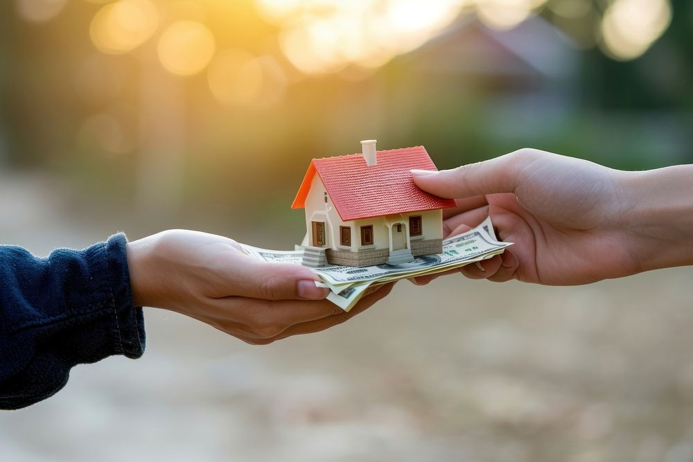 Photo of a hand offering a miniature house in exchange with a hand offering a money finger togetherness architecture.
