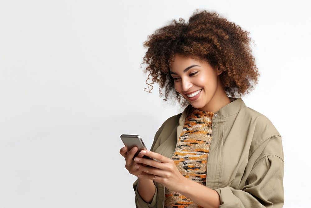 Positive curly haired ethnic woman uses mobile phone checks messages and reads news holds modern cellular in hands smile…