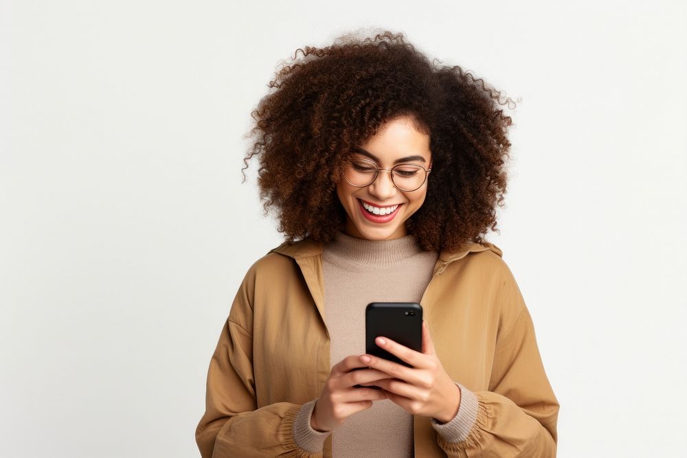 Positive curly haired ethnic woman uses mobile phone checks messages and reads news holds modern cellular in hands laughing…