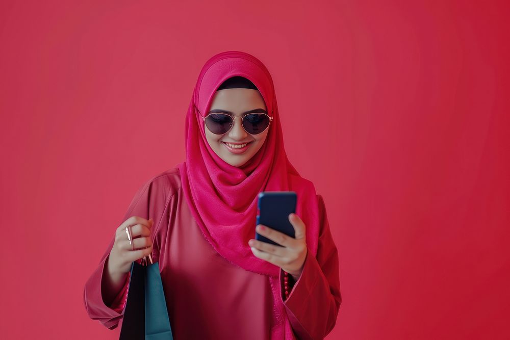 Smiling muslim mature woman wear sunglasses using her smartphone scarf red photographing.