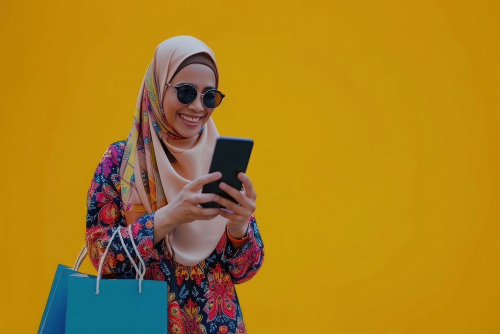 Smiling muslim mature woman wear sunglasses using her smartphone portability technology telephone.