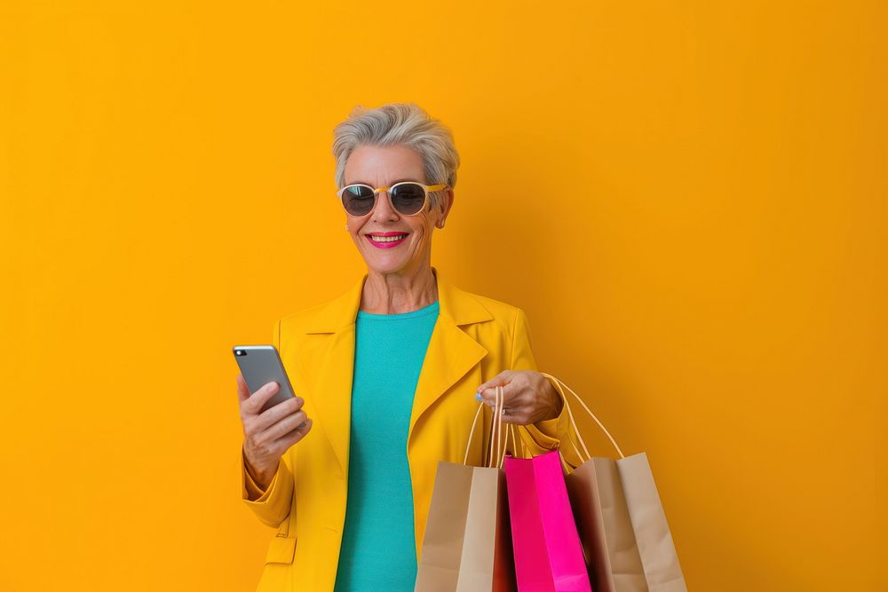 Smiling mature woman wear sunglasses using her smartphone bag adult shopping bag.