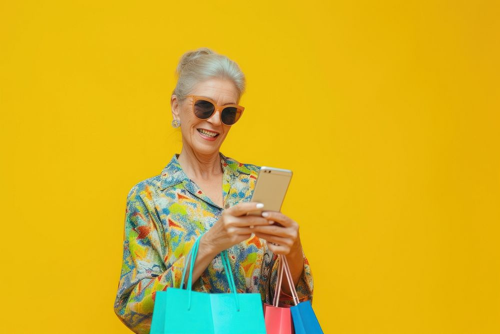 Smiling mature woman wear sunglasses using her smartphone adult bag shopping bag.
