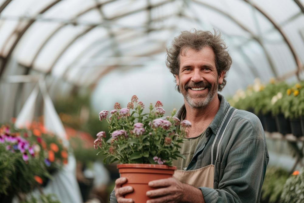 Man nursery owner with pot of flowers greenhouse gardening outdoors.