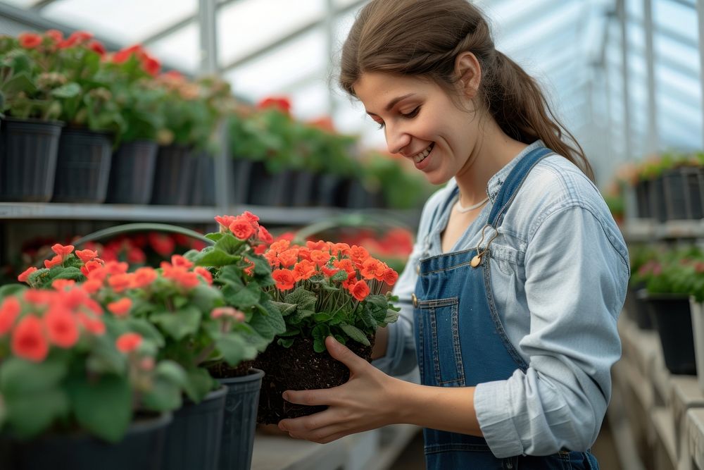 Female nursery owner with pot of flowers greenhouse gardening outdoors.