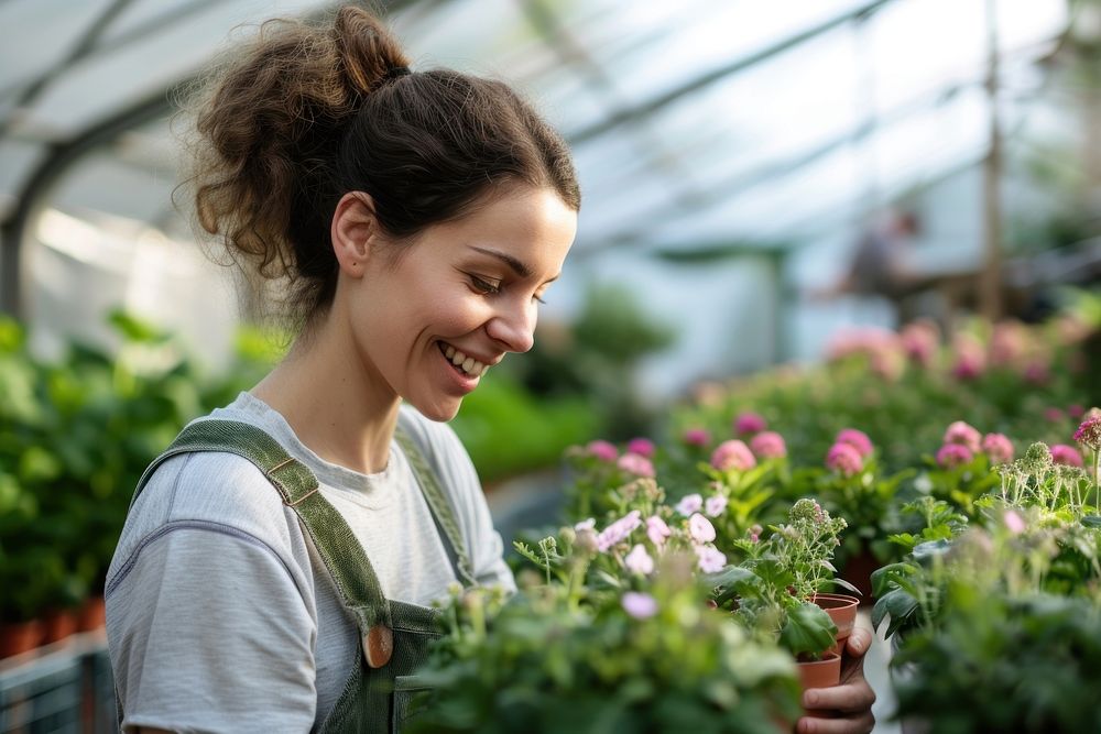 Female nursery owner with pot of flowers greenhouse gardening outdoors.