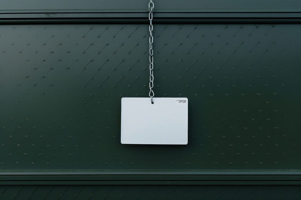 A business card is hanging on a black grid fence green white text.