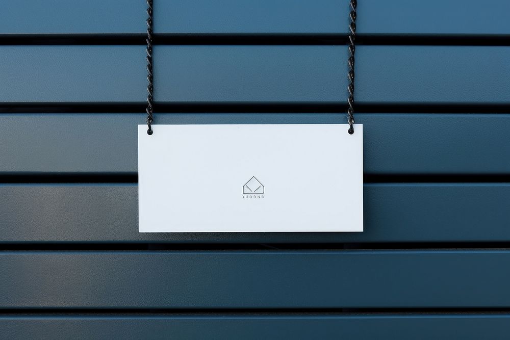 A business card is hanging on a black grid fence white text wall.