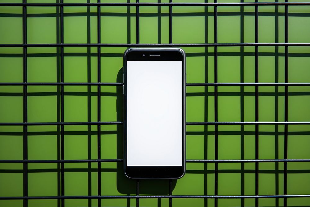 A smart phone on a black grid fence green wall architecture.