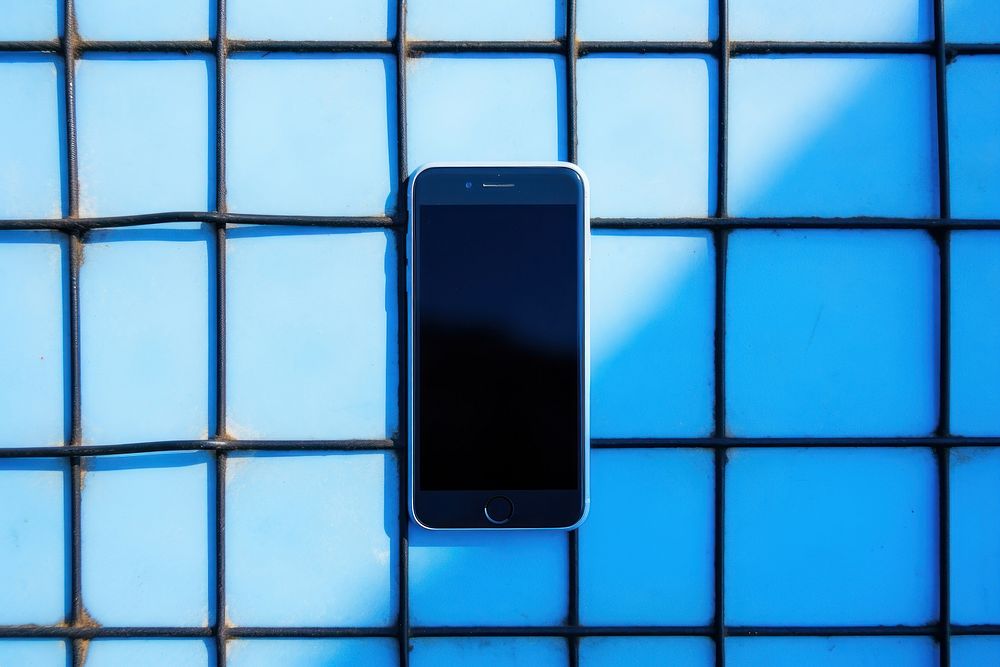 A smartphone is hanging on a black grid fence blue wall electronics.