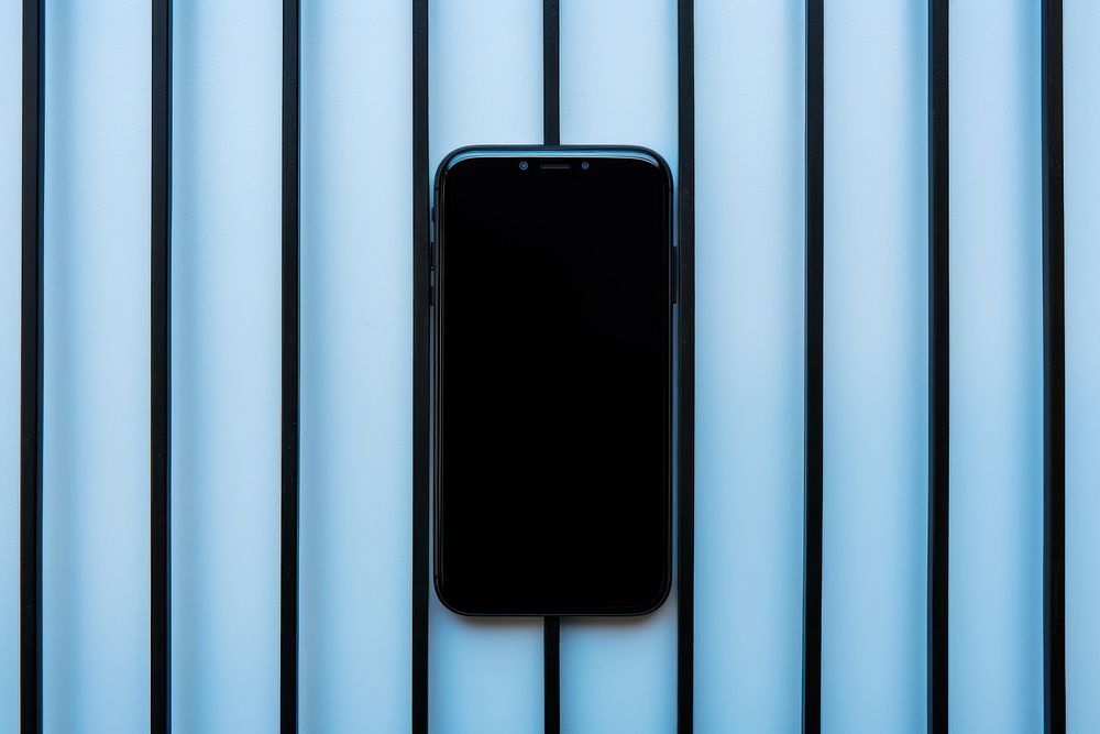 A smartphone is hanging on a black grid fence blue wall architecture.