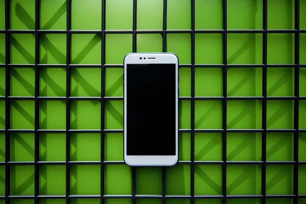 A smartphone on a black grid fence green wall electronics.