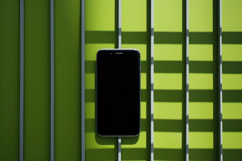 A smartphone on a black grid fence green wall portability.