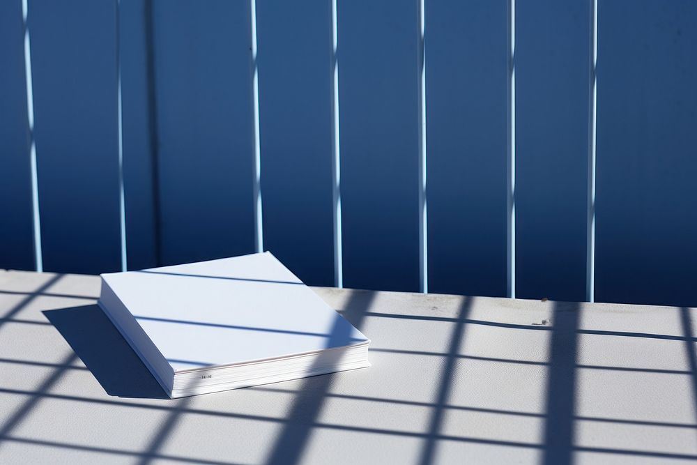 A white book is on a black grid fence blue wall architecture.