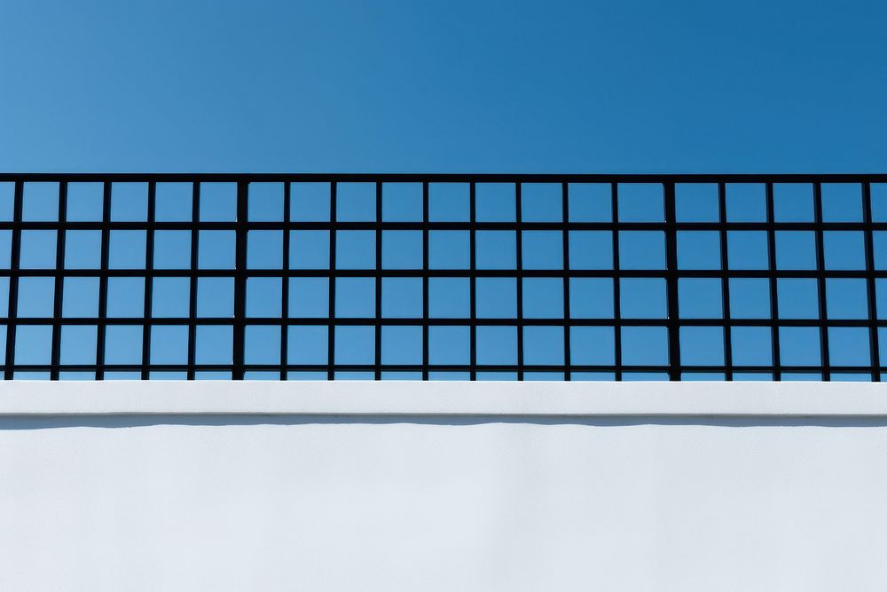 A black grid fence white wall blue.