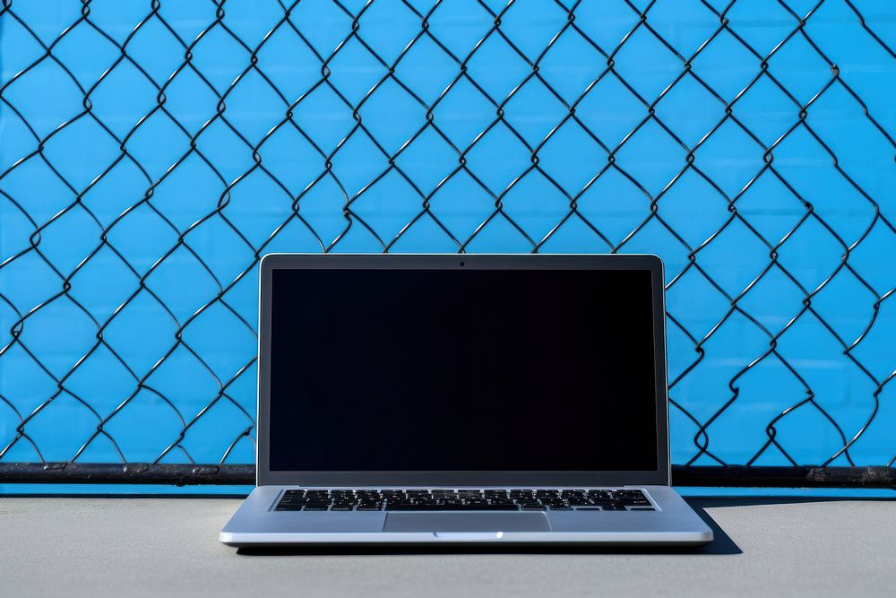A laptop is on a black grid fence computer wall blue.