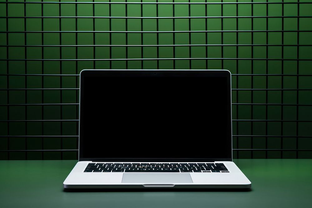 A laptop is on a black grid fence computer screen green.