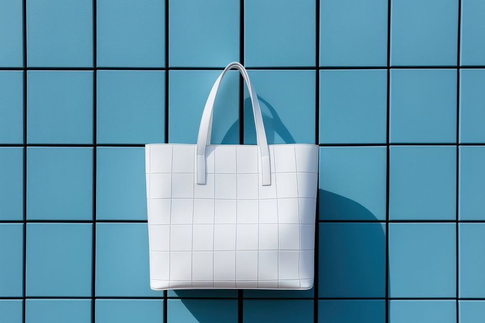 A white tote bag is hanging on a black grid fence handbag wall blue.