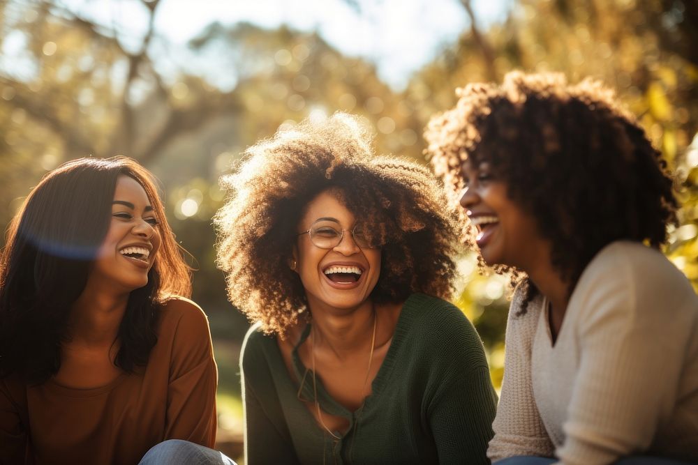 Three black women laughing sunlight outdoors.