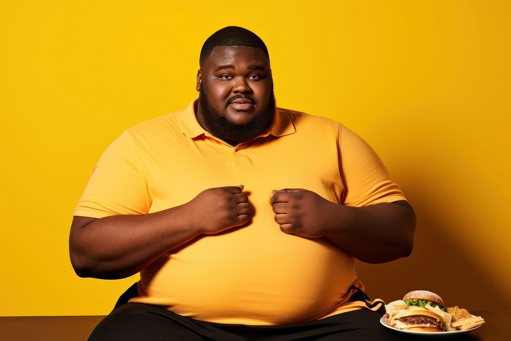 Big man putting his hand on his belly adult yellow background portrait.