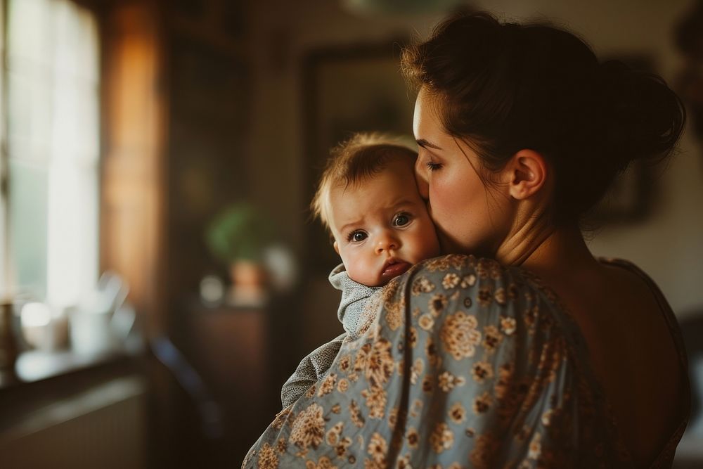 A loving american mother kissing her adorable little baby boy cradled in her arms at home photography portrait togetherness.