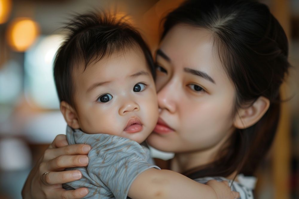 A loving asian mother kissing her adorable little baby boy cradled in her arms at home photography portrait child.