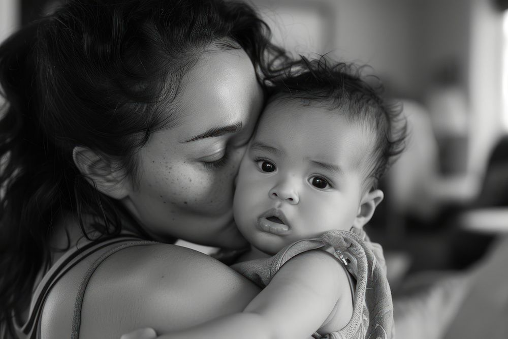 A loving mother kissing her adorable little baby boy cradled in her arms at home photography portrait hugging.