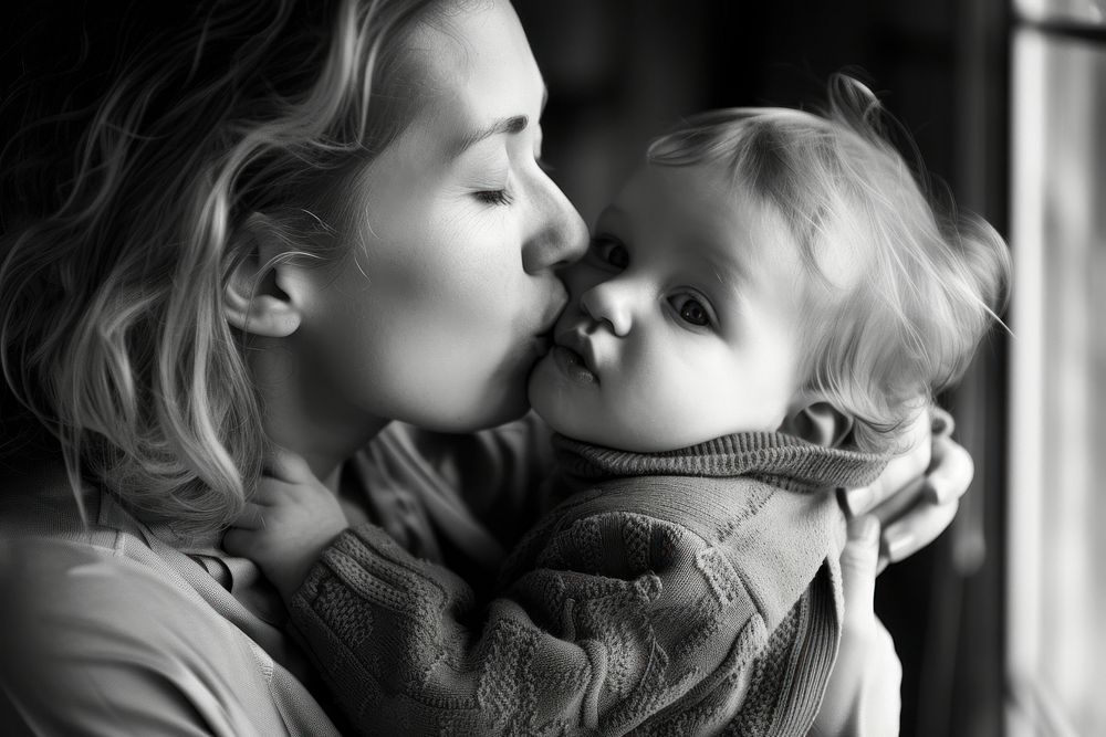 A loving mother kissing her adorable little baby boy cradled in her arms at home photography portrait hugging.