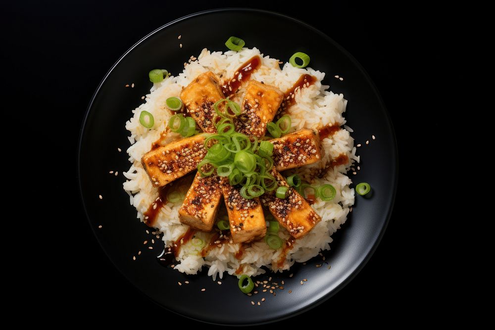 A rice and fried tofu with sesame seeds on the black plate food seafood meat.