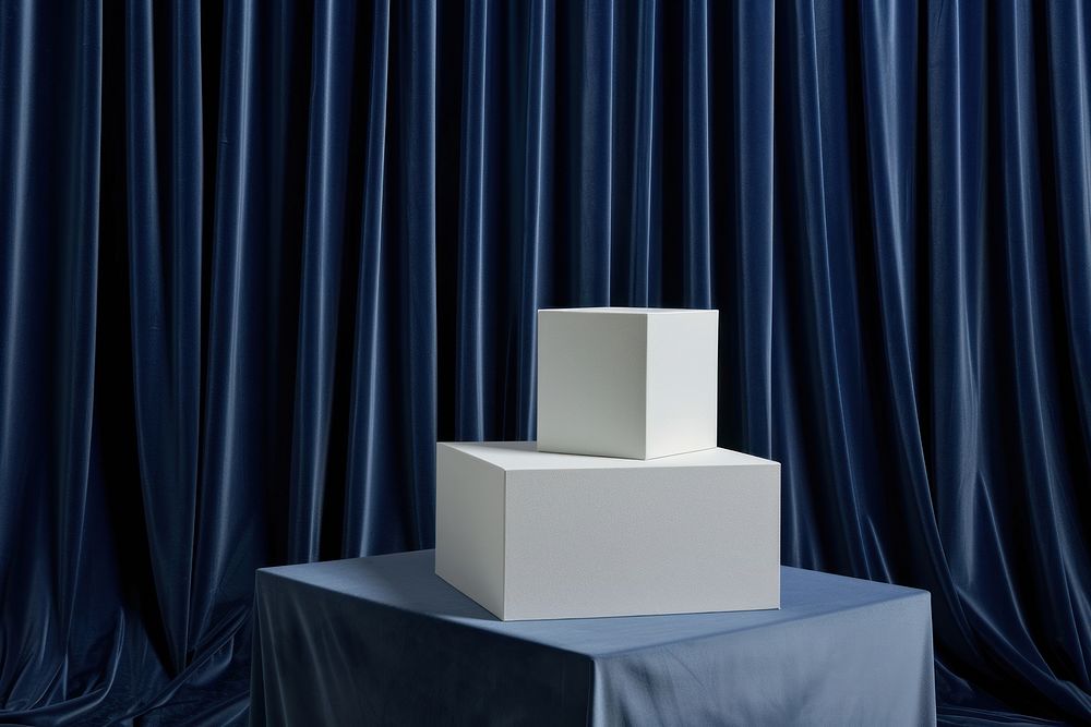 Two stacked white boxes on a podium backdrop curtain blue architecture.