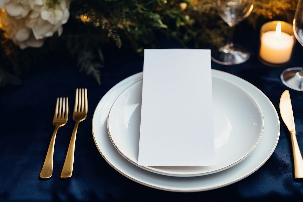 Paper white blank menu card on white plate napkin candle fork.