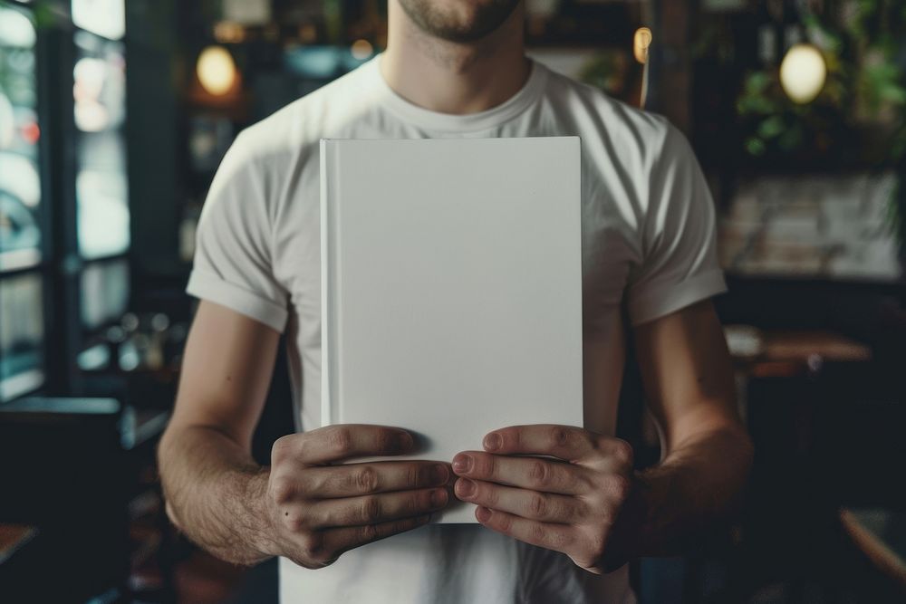 White man reading empty white book and show cover book up in front view midsection portrait clothing.