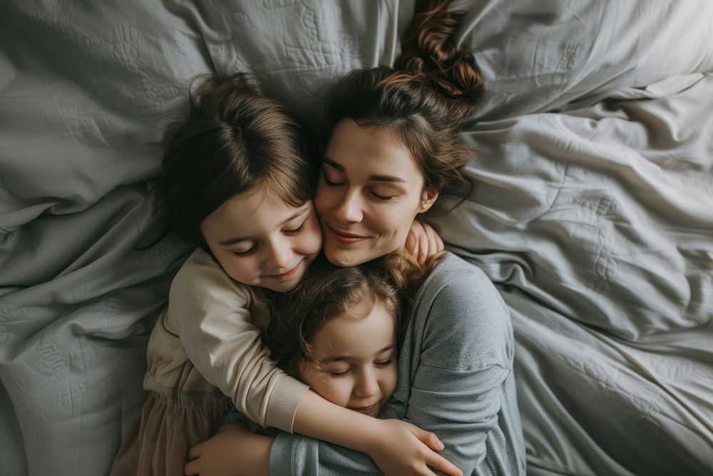 Woman hugging 2 girl children on gray bed blanket adult togetherness.
