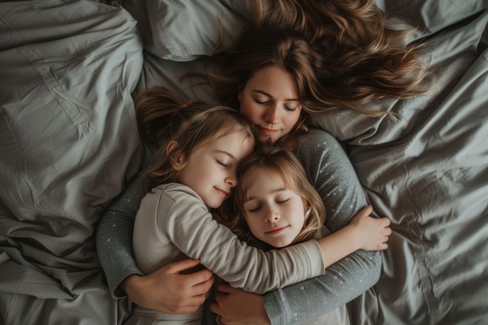 Woman hugging 2 girl children on gray bed blanket adult togetherness.