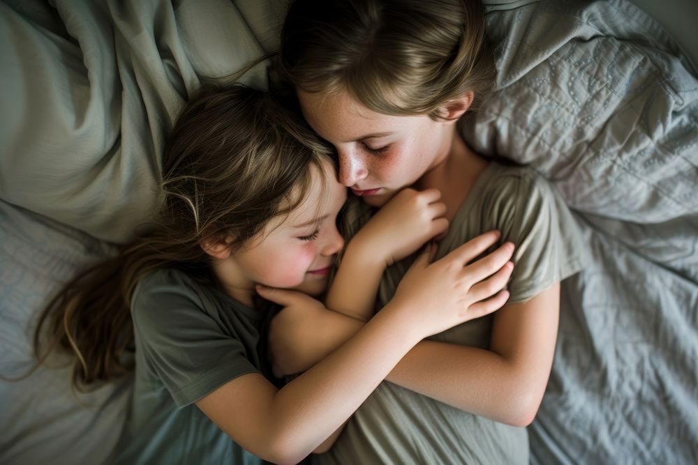 Mother hugging 2 girl children on gray bed togetherness affectionate comfortable.