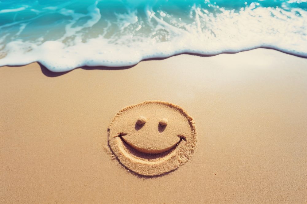 Smile icon written on sand beach backgrounds outdoors.