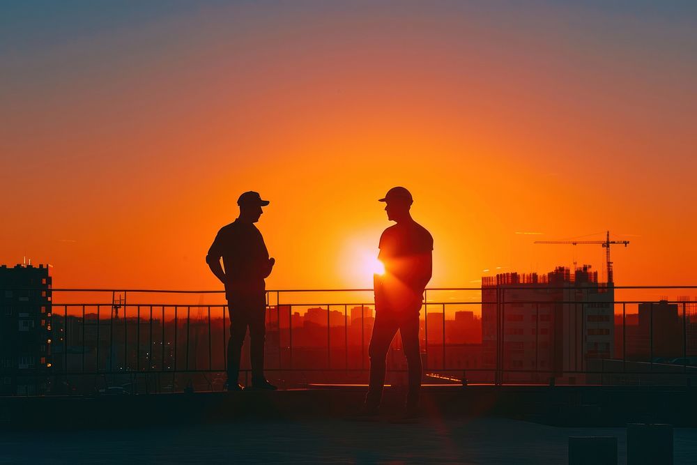 Engineers talking next to construction site backlighting silhouette sunset.
